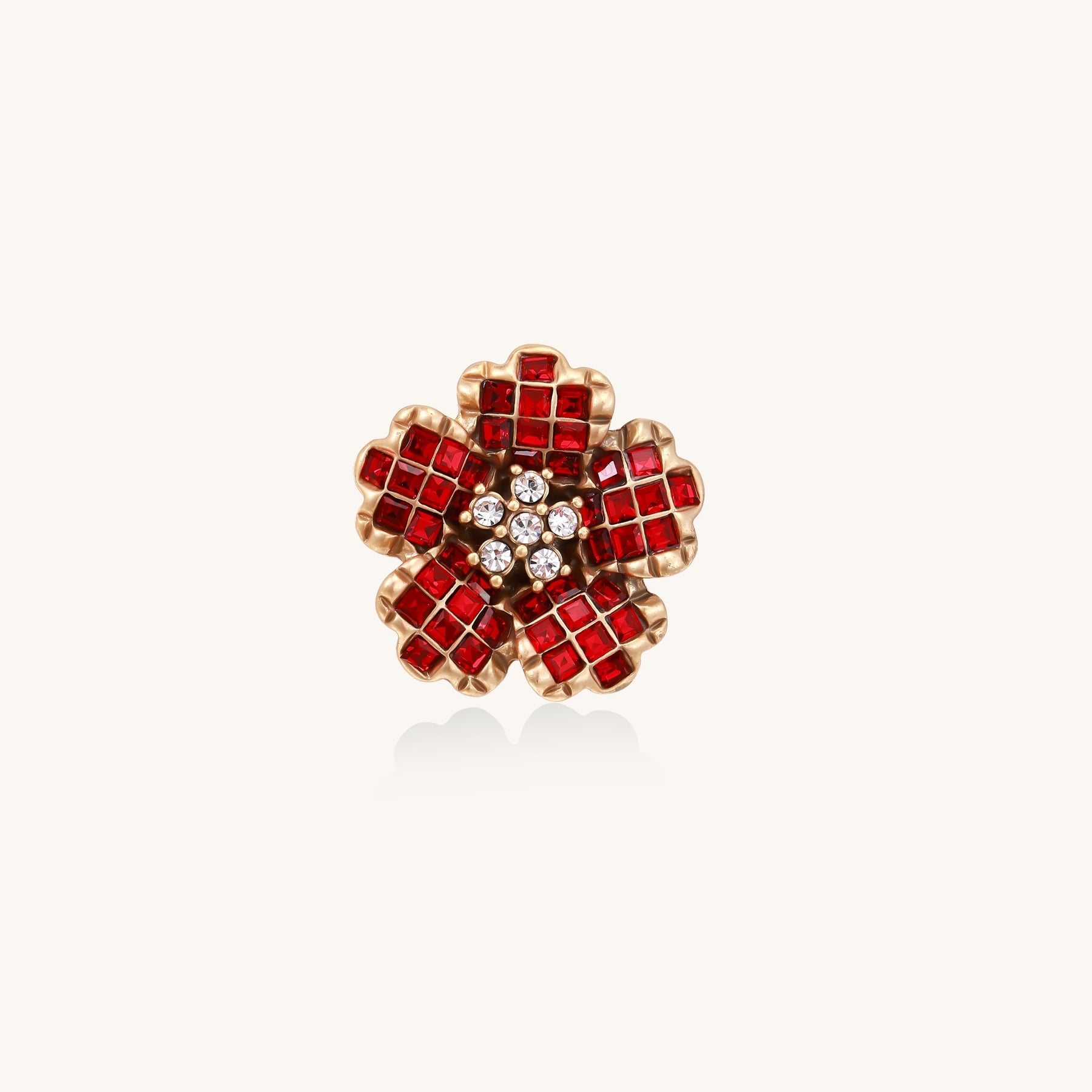 Statement ring with layered red crystal petals in gold-plated setting resembling a blooming flower on neutral background.