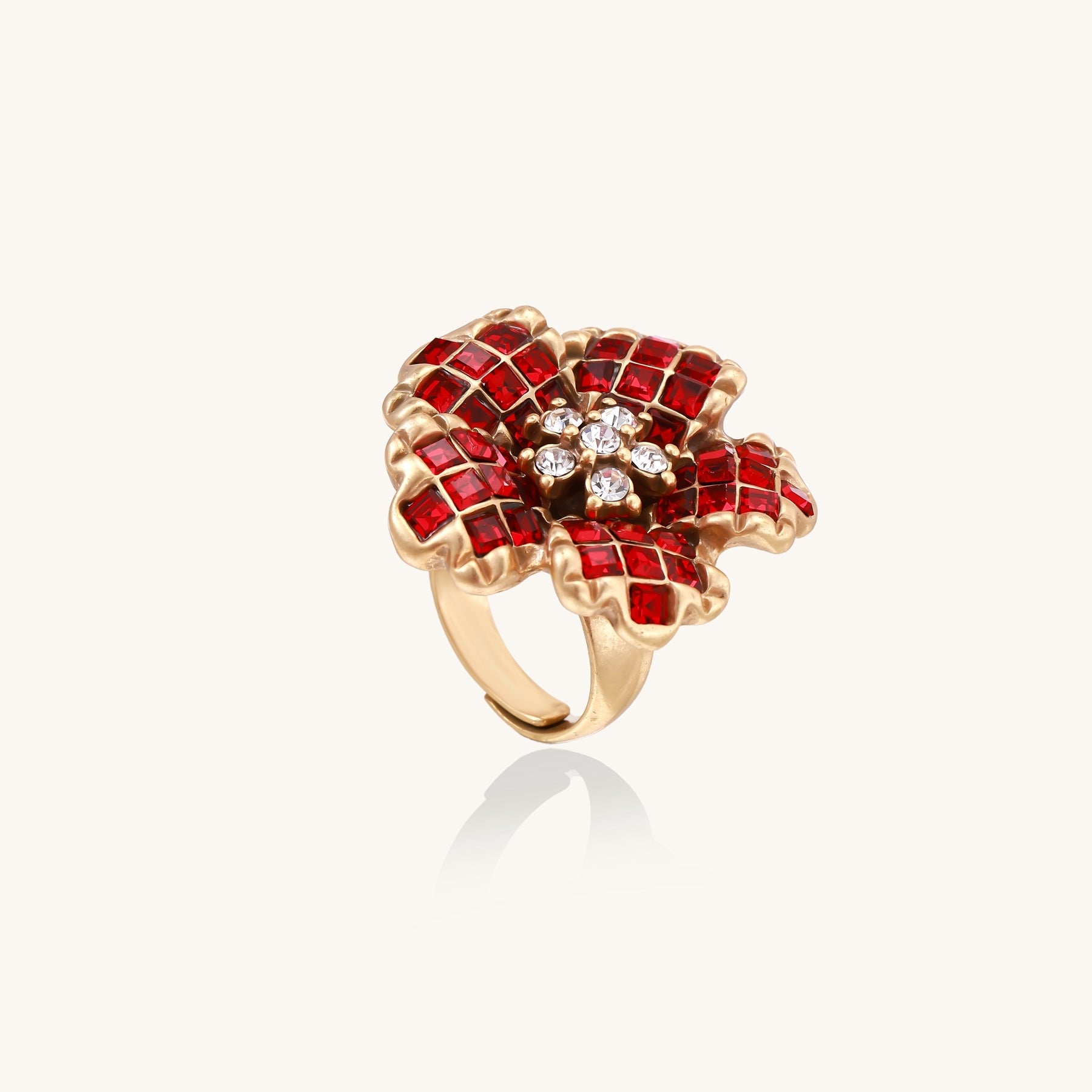 Statement ring with layered red crystal petals in gold-plated setting resembling a blooming flower on neutral background.