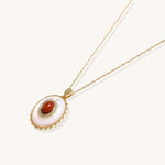 Oval gold-plated pendant featuring mother-of-pearl base with carnelian center stone and crystal accents on delicate chain
