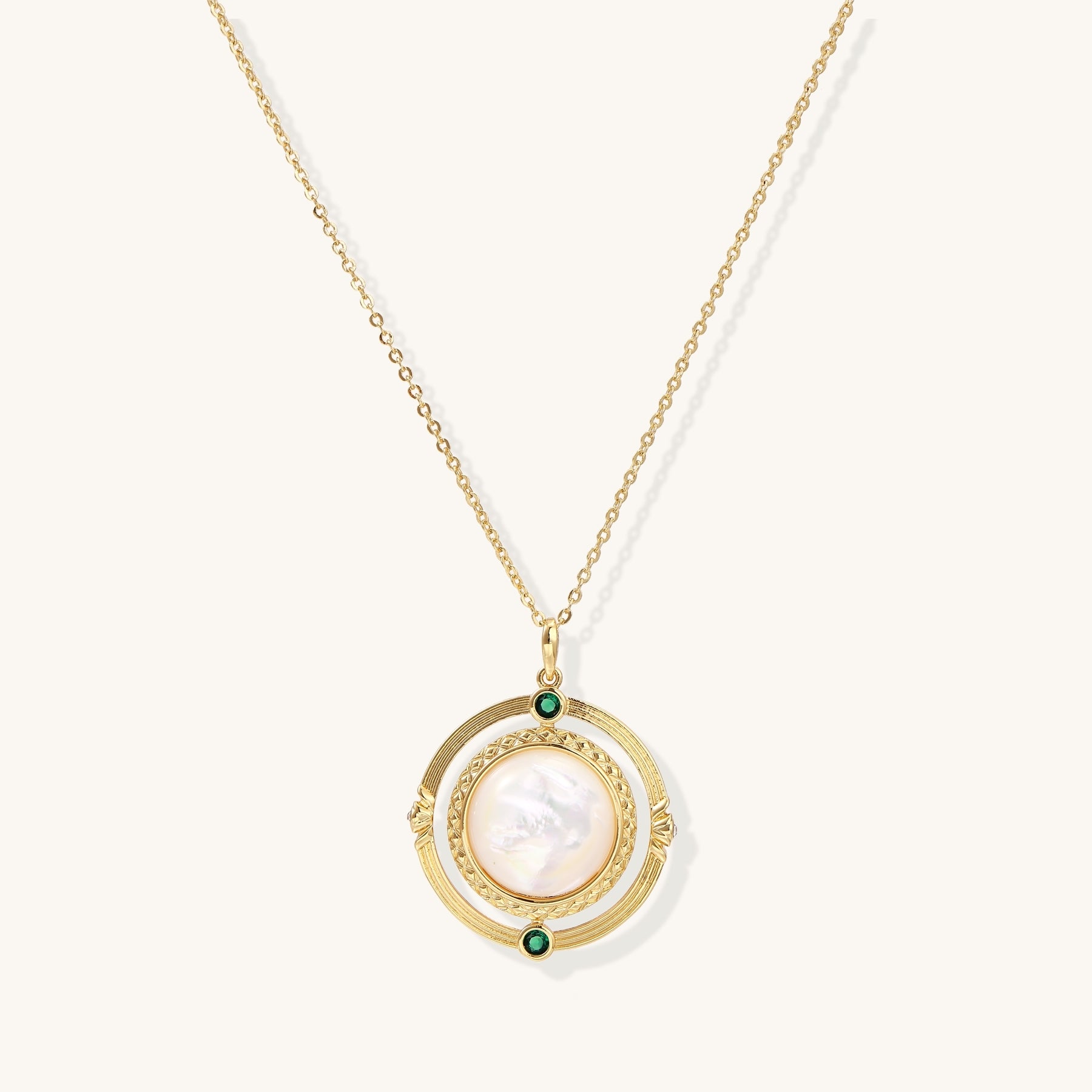 Gold-plated pendant necklace with circular orbital design, iridescent mother-of-pearl center and green zirconia accents