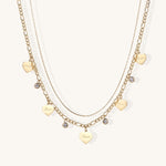 Two layered gold-plated necklaces with heart pendants engraved 'Love' and sparkling crystal charms on white background.