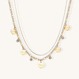 Two layered gold-plated necklaces with heart pendants engraved 'Love' and sparkling crystal charms on white background.
