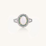 Gold-plated ring with oval cat's eye stone center, blue accent stones, and crystal halo on white background.