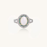 Gold-plated ring with oval cat's eye stone center, blue accent stones, and crystal halo on white background.