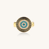 Gold-plated brass ring with Greek key border, evil eye center, and turquoise cubic zirconia stones in chunky chain band style.