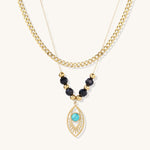 Gold layered necklace set with evil eye pendant, turquoise center stone, and black beaded chain on cream background