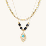 Gold layered necklace set with evil eye pendant, turquoise center stone, and black beaded chain on cream background