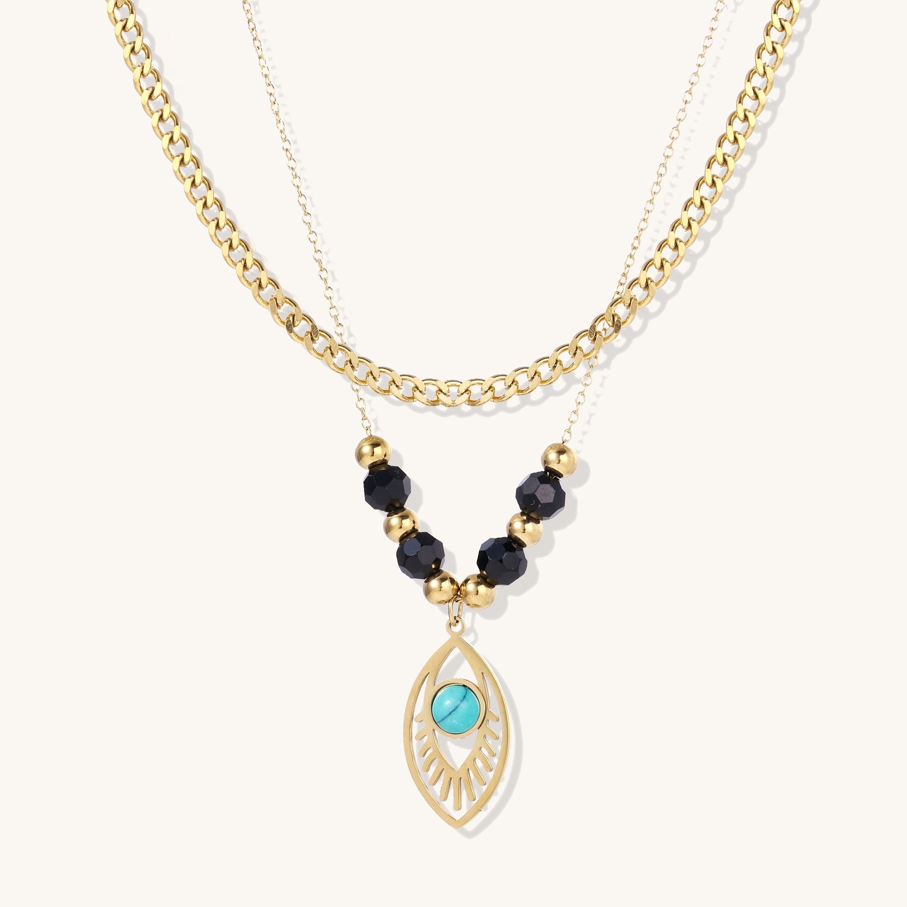 Gold layered necklace set with evil eye pendant, turquoise center stone, and black beaded chain on cream background