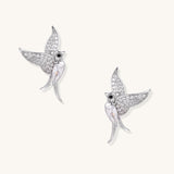 Pair of gold-plated hummingbird earrings with crystal pavé wings and black stone eyes on neutral background.