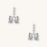 Delicate gold-plated bow drop earrings with three zirconia crystals and center pearl on white background.