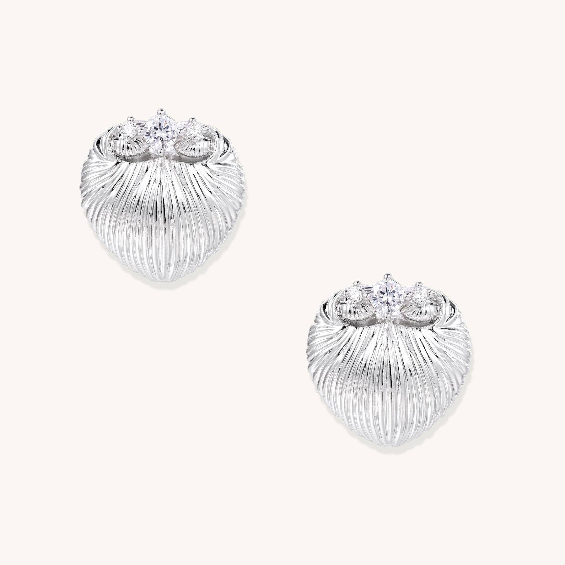 Pair of gold-plated heart-shaped earrings with vertical ribbed texture and sparkling zirconia stones at top on white background.
