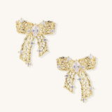 Gold and silver bow-shaped earrings with intricate lattice pattern and clear zirconia stones on neutral background.