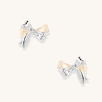 Close-up of bow-shaped stud earrings with 18K gold plated brass and silver details on white background.