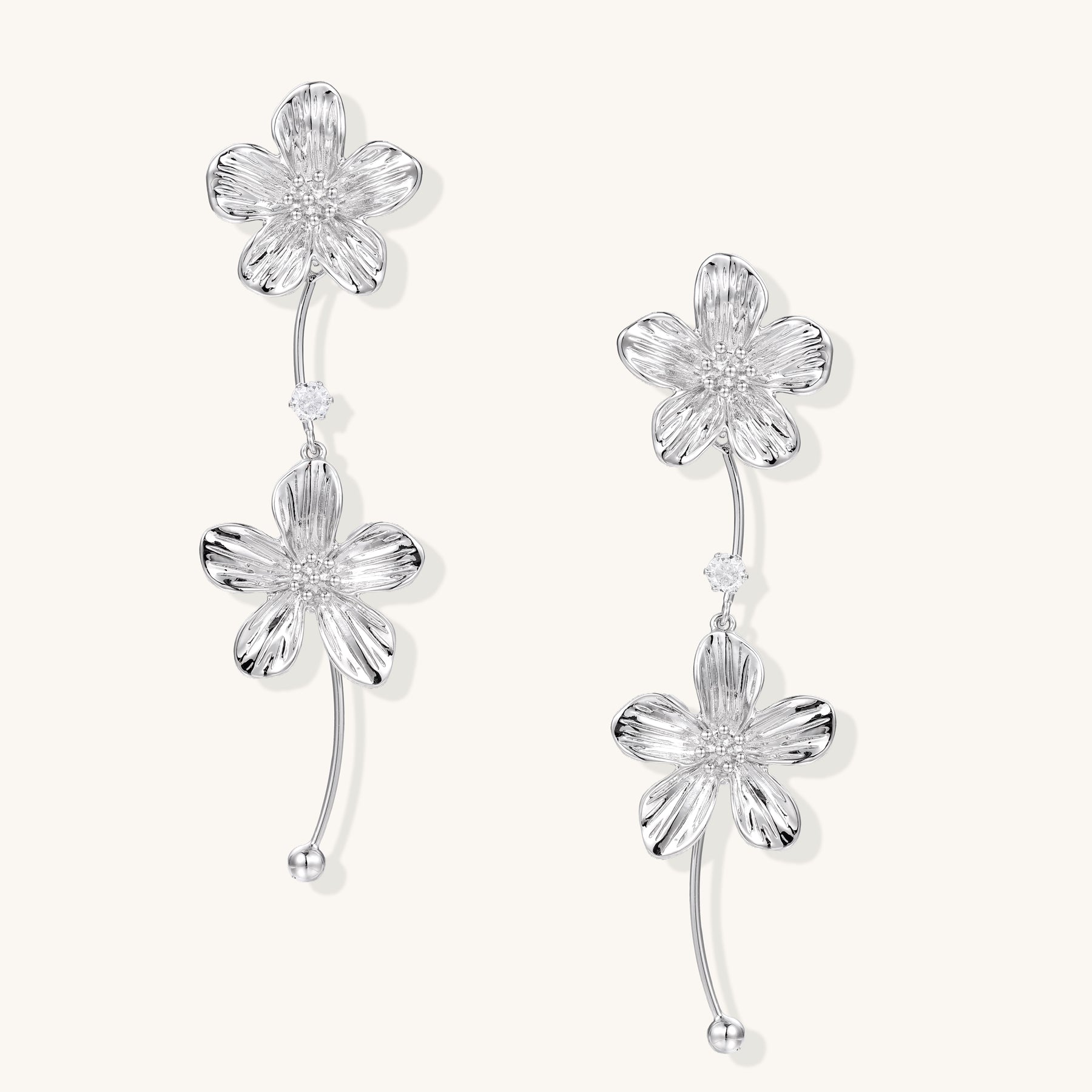 Gold-plated floral dangle earrings with zirconia crystal centers and curved stems on white background.