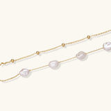 Double-strand gold bracelet with irregular baroque pearls and smooth freshwater pearls on cream background.