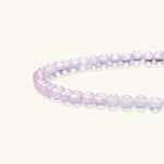 Double-wrap lavender beaded bracelet with rose quartz, pearls, gold vermeil charm and pink tassel on white background.