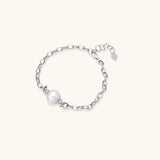 Rhodium-plated silver chain bracelet with single white freshwater pearl and heart charm clasp on cream background