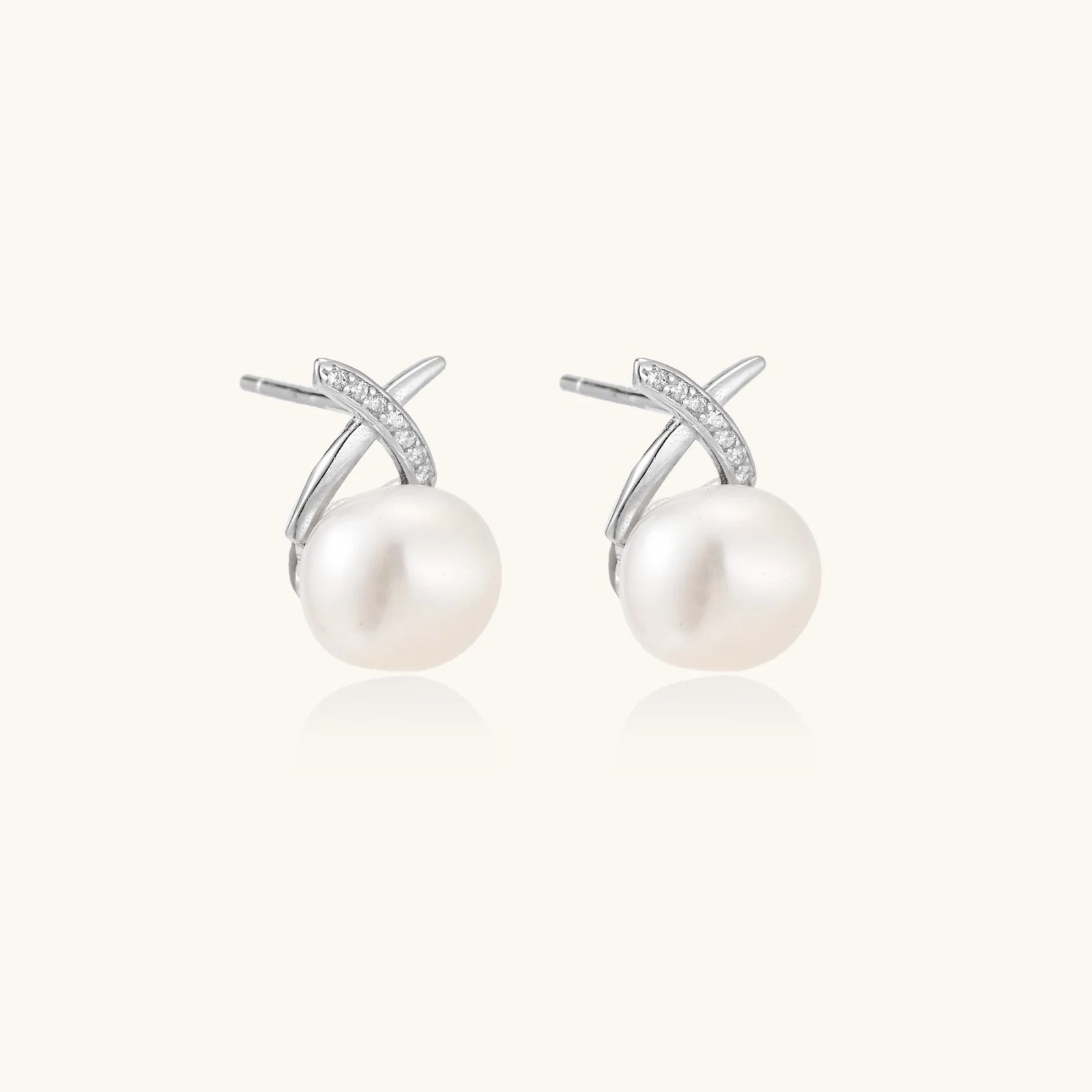 Rhodium-plated silver stud earrings with sparkling X design above lustrous round freshwater pearls on white background.