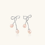 Rhodium-plated silver earrings with organic vine curves and two peachy freshwater pearls on cream background