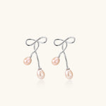 Rhodium-plated silver earrings with organic vine curves and two peachy freshwater pearls on cream background