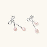 Rhodium-plated silver earrings with organic vine curves and two peachy freshwater pearls on cream background