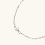 Dainty rhodium-plated silver chain necklace with centered 10mm freshwater pearl and crystal accents on cream background