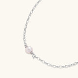 Dainty rhodium-plated silver chain necklace with centered 10mm freshwater pearl and crystal accents on cream background