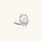 Silver ring with lustrous white pearl center surrounded by sparkling crystal halo on light background.