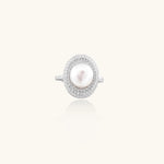Silver ring with lustrous white pearl center surrounded by sparkling crystal halo on light background.