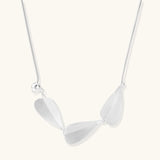 Minimalist sterling silver necklace with three brushed leaf-shaped pendants on delicate chain against white background