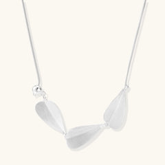 Minimalist sterling silver necklace with three brushed leaf-shaped pendants on delicate chain against white background