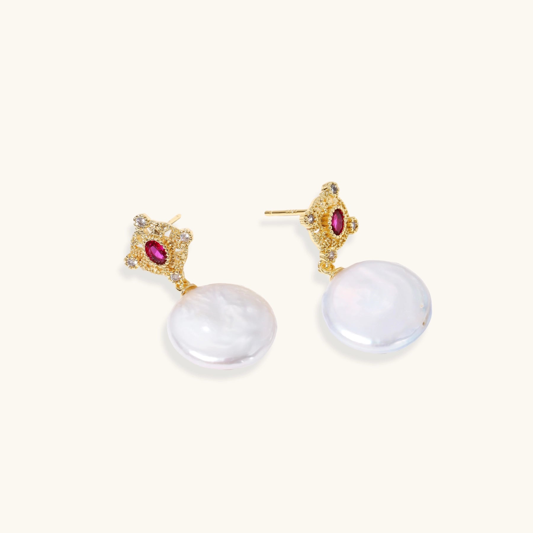 Gold baroque pearl earrings with pink gemstone studs and ornate detailing on cream background.