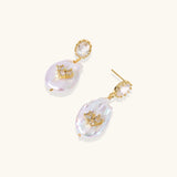 Gold-plated drop earrings with iridescent baroque pearls and crystal flower accents on cream background
