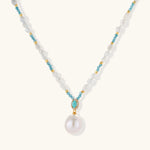 Beaded necklace with baroque pearls, turquoise stones, and gold accents featuring a large pearl pendant on white background.