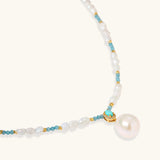 Beaded necklace with baroque pearls, turquoise stones, and gold accents featuring a large pearl pendant on white background.