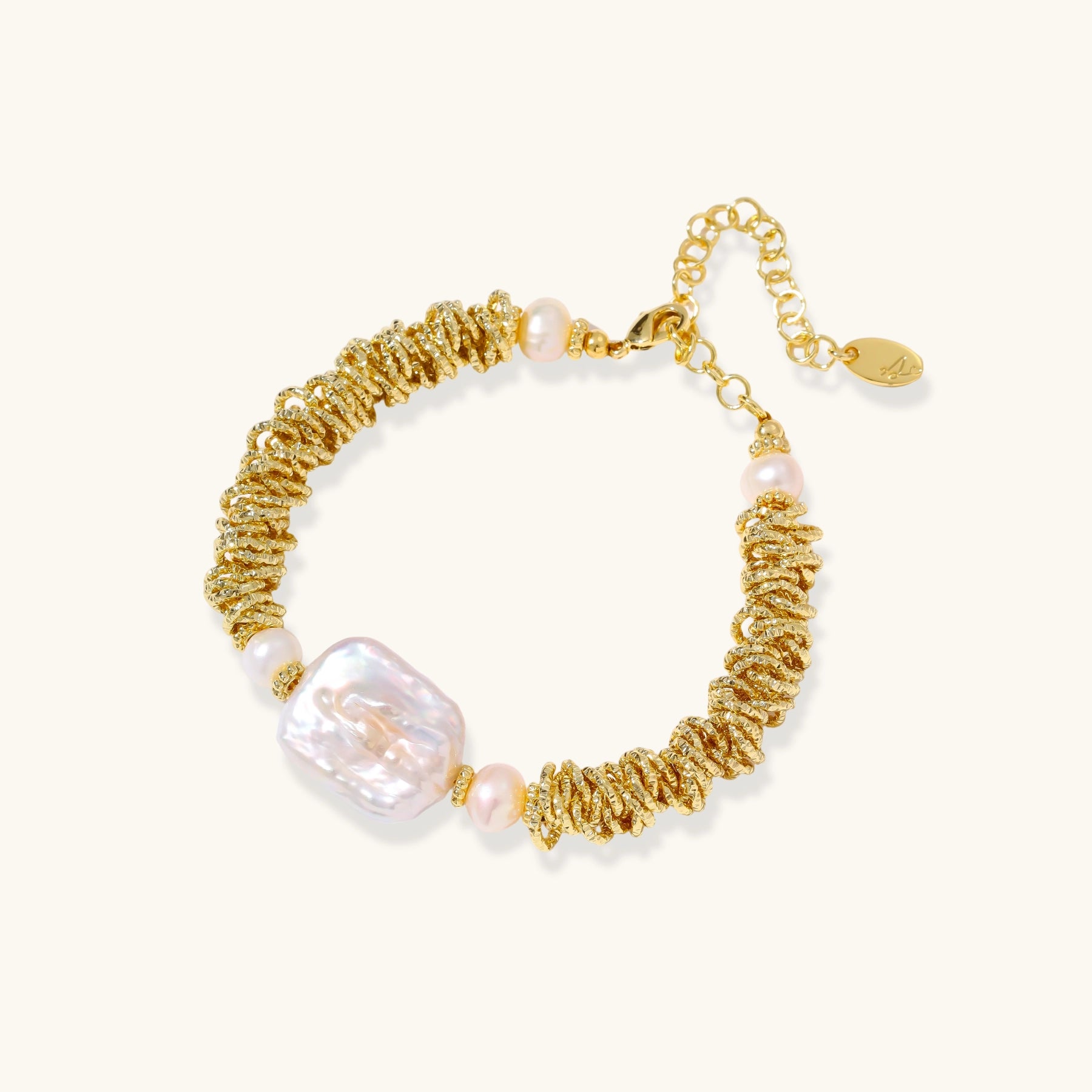 18k gold-plated bracelet with textured wave segments, baroque pearl centerpiece, and round freshwater pearls on cream background
