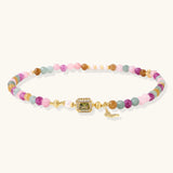 Stretchable bracelet with pastel gemstone beads, freshwater pearls, gold centerpiece and butterfly charm on cream background