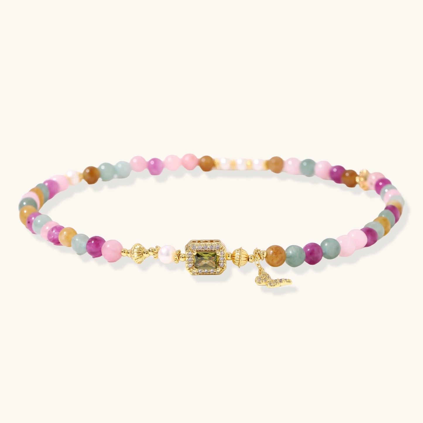 Stretchable bracelet with pastel gemstone beads, freshwater pearls, gold centerpiece and butterfly charm on cream background