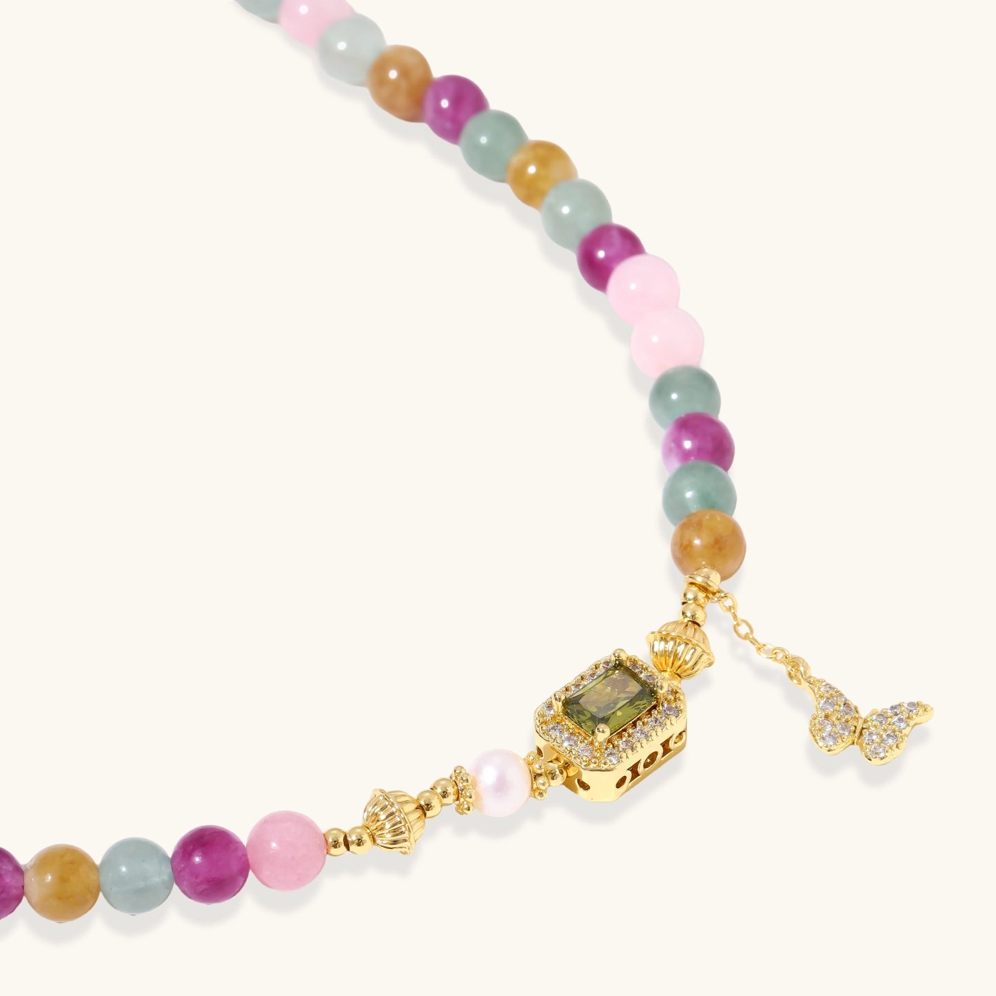 Stretchable bracelet with pastel gemstone beads, freshwater pearls, gold centerpiece and butterfly charm on cream background