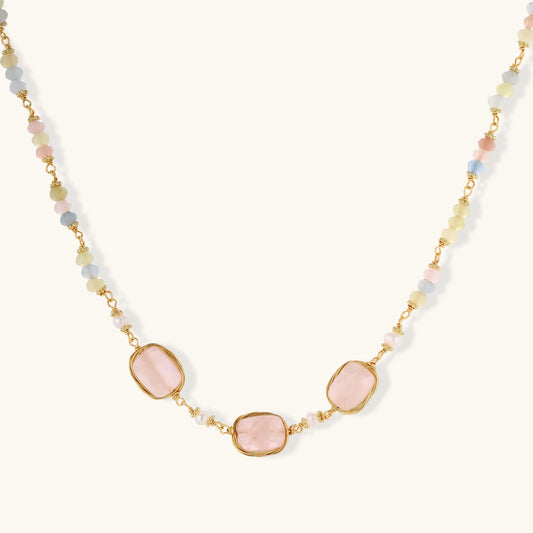 Gold necklace with three rose quartz stones, multicolor pastel beads, and pearl accents on white background.