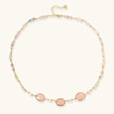 Gold necklace with three rose quartz stones, multicolor pastel beads, and pearl accents on white background.