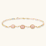 Gold necklace with three rose quartz stones, multicolor pastel beads, and pearl accents on white background.