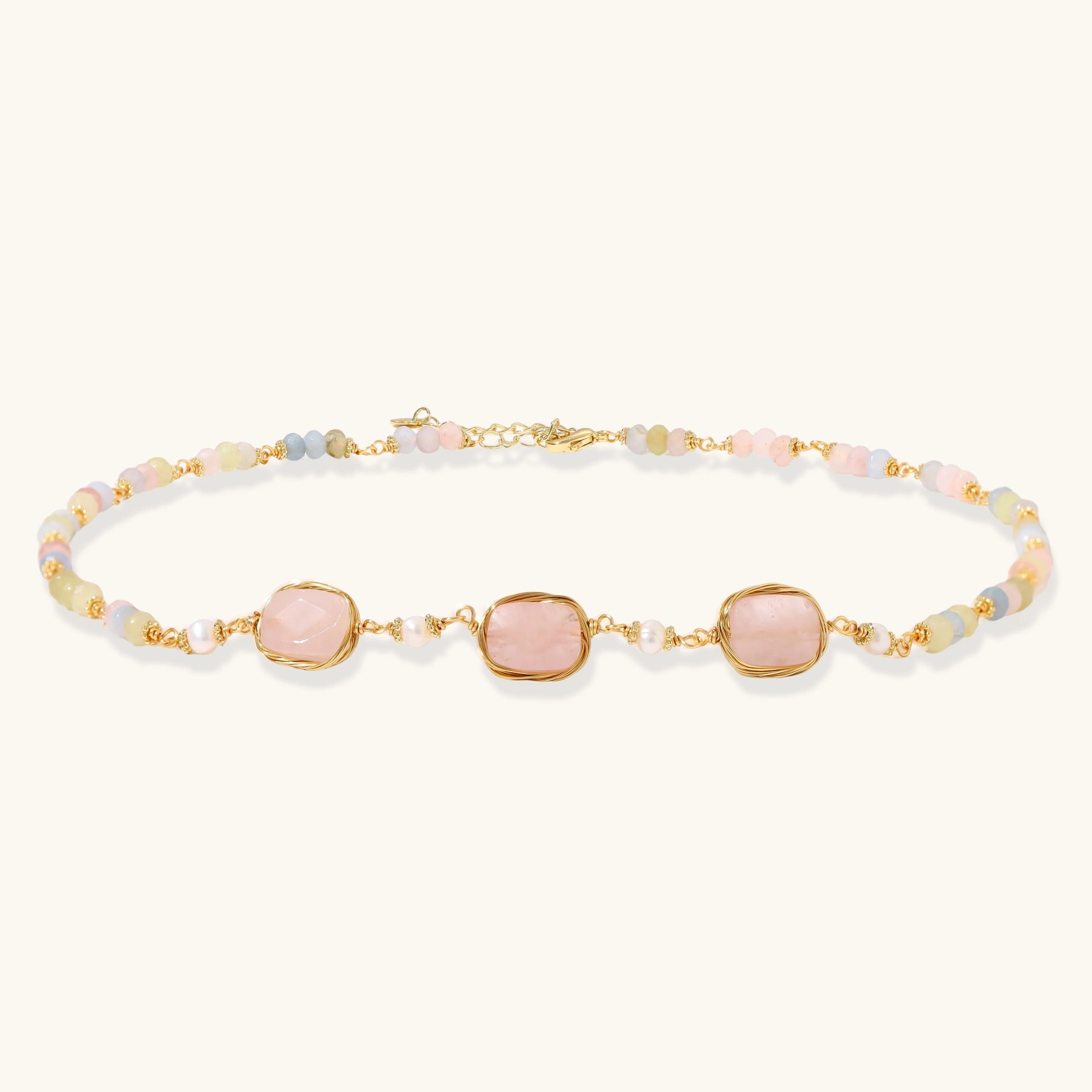 Gold necklace with three rose quartz stones, multicolor pastel beads, and pearl accents on white background.