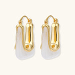 Sculptural gold-plated hoop earrings with flowing curved design and lever-back closure on cream background.