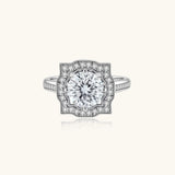 Sterling silver ring with round moissanite center stone in ornate scalloped halo setting on white background.