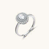 Sterling silver ring with oval moissanite center stone surrounded by double halo of sparkling stones on neutral background.