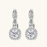 Sterling silver twisted hoop earrings with round moissanite stones in halo settings against neutral background.