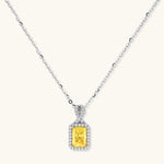 Rectangular yellow moissanite pendant in sterling silver halo setting on delicate chain against cream background.