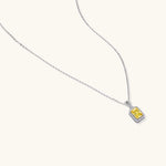 Rectangular yellow moissanite pendant in sterling silver halo setting on delicate chain against cream background.