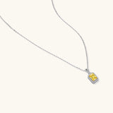 Rectangular yellow moissanite pendant in sterling silver halo setting on delicate chain against cream background.